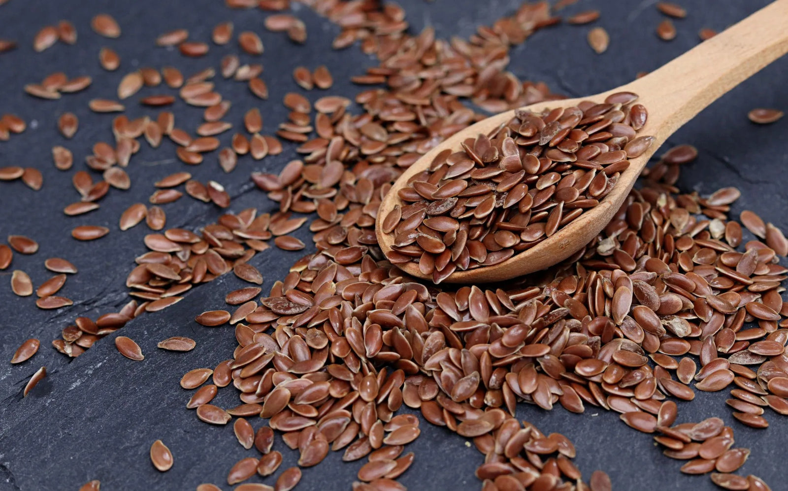 A wooden spoon holding brown flaxseeds, ready to measure the right amount of flaxseed to feed a horse.